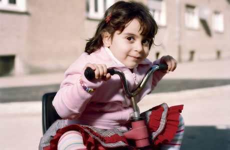 Ein Mädchen sitzt im Freien auf einem Dreirad und schaut in die Kamera.