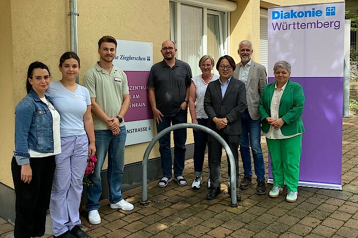 Eine Gruppe von 8 Personen steht vor einem Pflegeheim. Alle lachen in die Kamera.