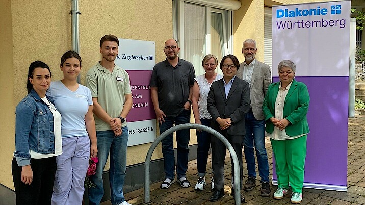 Eine Gruppe von 8 Personen steht vor einem Pflegeheim. Alle lachen in die Kamera.
