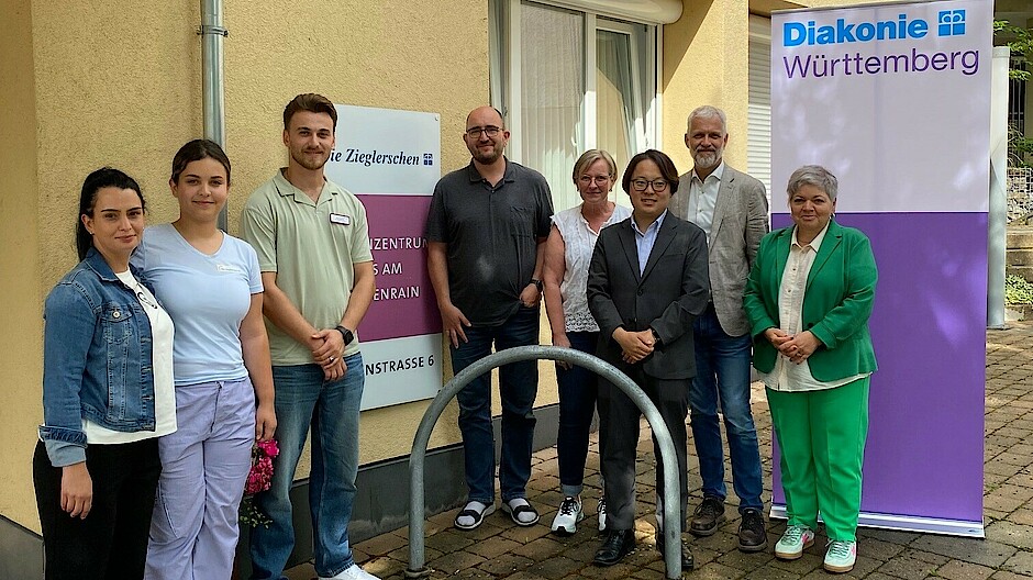 Eine Gruppe von 8 Personen steht vor einem Pflegeheim. Alle lachen in die Kamera.