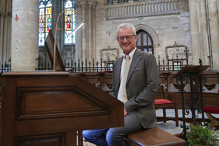 Hans-Jürgen Kaiser sitzt im Anzug an der Orgel in der Kirche und lächelt.