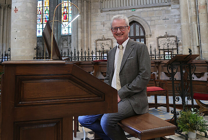 Hans-Jürgen Kaiser sitzt im Anzug an der Orgel in der Kirche und lächelt.