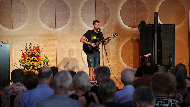 Maexla steht mit Gitarre vor dem Publikum.