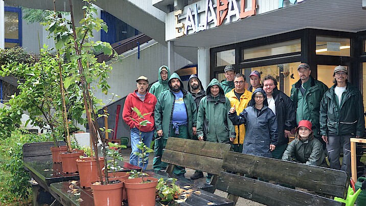 Die Garten- und Landschaftsbaugruppe steht in regenfester Arbeitskleidung hinter einigen Jungpflanzen auf einem Tisch