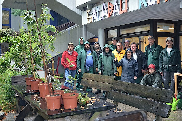 Die Garten- und Landschaftsbaugruppe steht in regenfester Arbeitskleidung hinter einigen Jungpflanzen auf einem Tisch