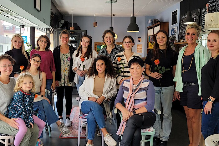 Fröhliche Frauen sitzen und stehen zum Gruppenfoto im Café
