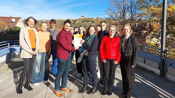 Bild zeigt ein Gruppenbild der Mitarbeiter der Einrichtung, die die Urkunde hoch halten