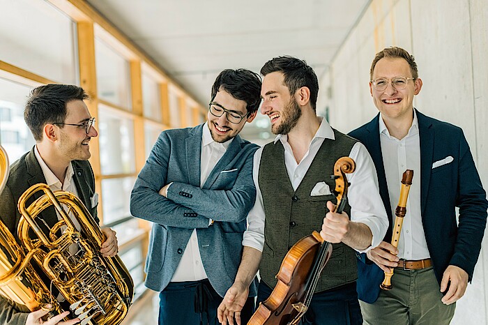 Die vier Brüder stehen zusammen da mit Instrumenten und lachen. 