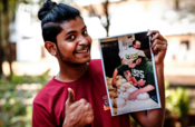 Ein junger indischer Mann gibt eine Daumen-Hoch-Zeichen und hält ein Foto von backenden Konfirmanden in der Hand.