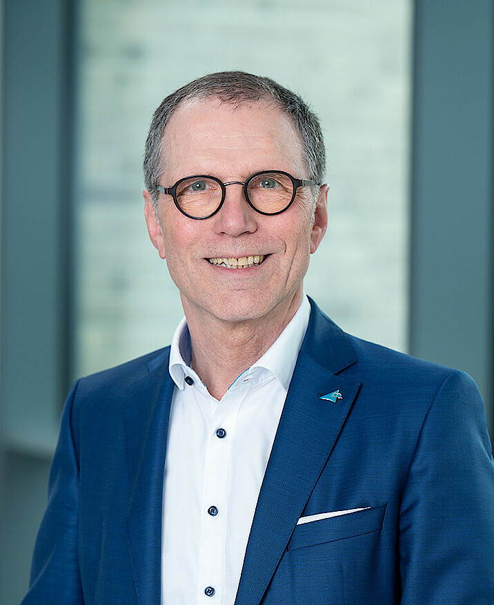 Das Bild zeigt ein Porträtfoto von Bernhard Schneider. Er trägt eine Brille und lächelt.