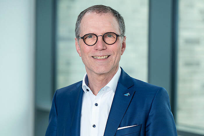 Das Bild zeigt ein Porträtfoto von Bernhard Schneider. Er trägt eine Brille und lächelt.