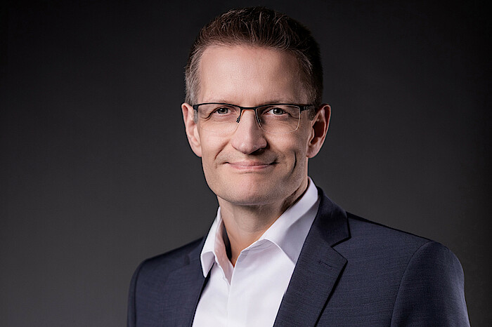 Dr. Dietmar Kauderer träg einen dunklen Anzug und ein weißes Hemd und lächelt.