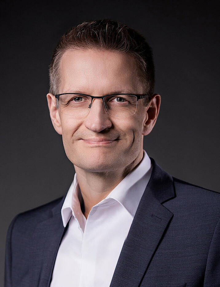 Dr. Dietmar Kauderer träg einen dunklen Anzug und ein weißes Hemd und lächelt.