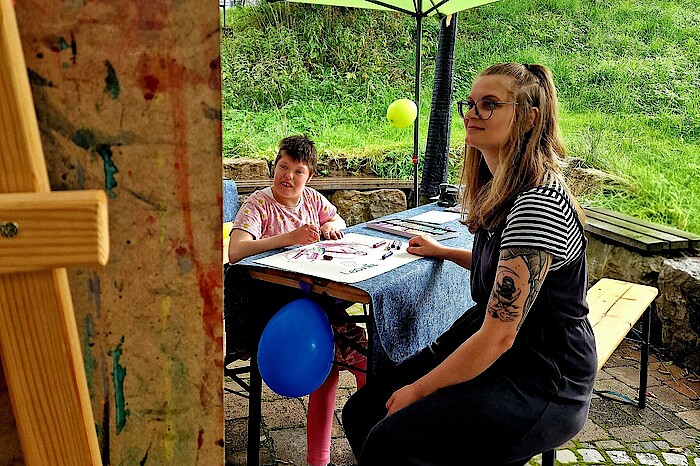 Eine Frau und ein Kind sitzen draußen an einem Tisch mit Malutensilien 