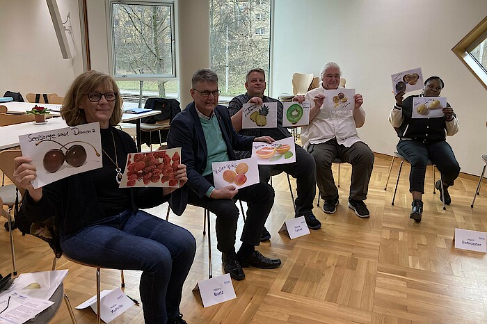 Kursteilnehmende halten Bilder von Früchten hoch.