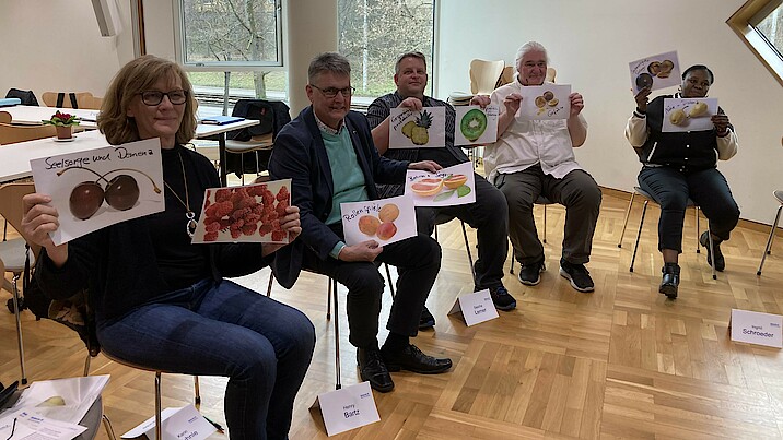 Kursteilnehmende halten Bilder von Früchten hoch.