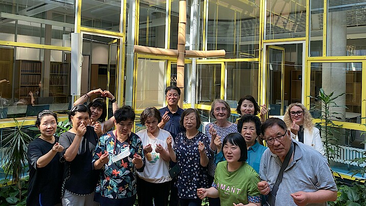 Die südkoreanische Gästegruppe steht vor dem Kreuz in der Landesgeschäftsstelle - mit den Händen werden Herzsymbole geformt.