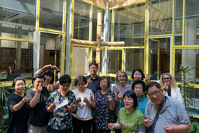 Die südkoreanische Gästegruppe steht vor dem Kreuz in der Landesgeschäftsstelle - mit den Händen werden Herzsymbole geformt.
