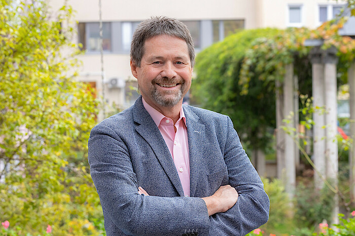 Ralf Horndasch steht lächelnd und mit verschränkten Armen da, er trägt ein graues Sakko.