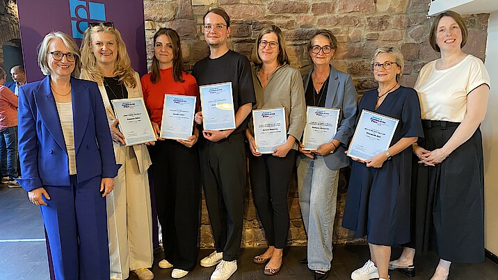 Die Gewinnerinnen und Gewinner des Diakonie Journalistenpreis 2025 stehen eingerahmt von den Vorständinnen der Diakonischen Werke Württemberg und Baden mit ihren Urkunden in der Hand vor einer Wand und lachen in die Kamera.