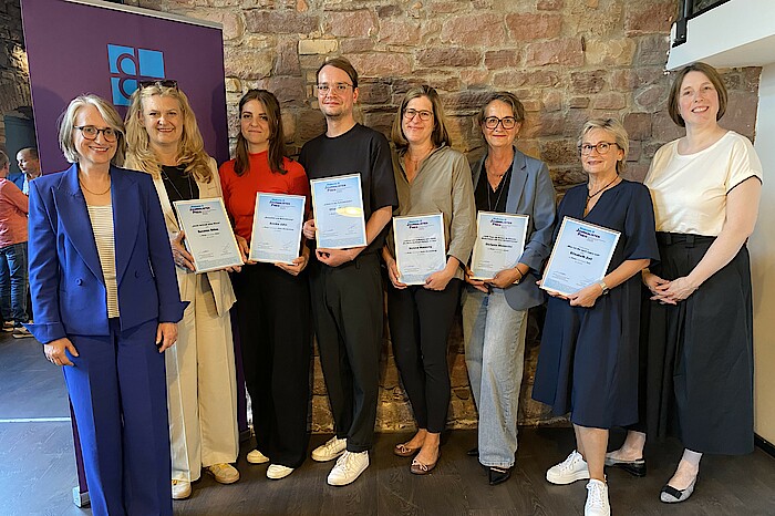 Die Gewinnerinnen und Gewinner des Diakonie Journalistenpreis 2025 stehen eingerahmt von den Vorständinnen der Diakonischen Werke Württemberg und Baden mit ihren Urkunden in der Hand vor einer Wand und lachen in die Kamera.