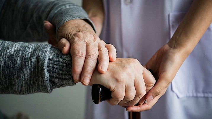 Pflegerin hält die Hand einer auf den Stock gestützten Frau.