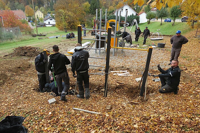 Menschen in schwarzer Arbeitskleidung bauen Spielgeräte auf.