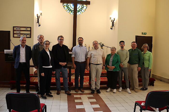 Eine Gruppe aus 10 Personen, bestehend aus Männer und Frauen, steht in einer Kirche vor einem Altar.