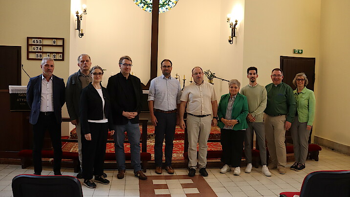 Eine Gruppe aus 10 Personen, bestehend aus Männer und Frauen, steht in einer Kirche vor einem Altar.
