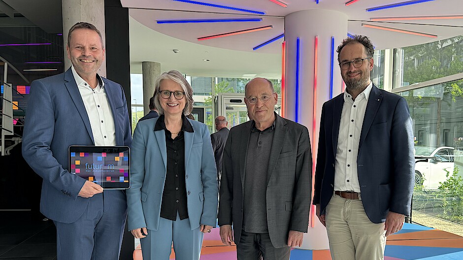 Finanzvorstand Dr. Robert Bachert, Vorstandsvorsitzende Dr. Annette Noller und sozialpolitischer Vorstand Dr. Kornelius Knapp stehen lächelnd neben Gregor Gysi im futurum