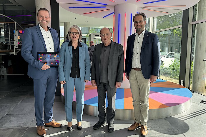 Finanzvorstand Dr. Robert Bachert, Vorstandsvorsitzende Dr. Annette Noller und sozialpolitischer Vorstand Dr. Kornelius Knapp stehen lächelnd neben Gregor Gysi im futurum