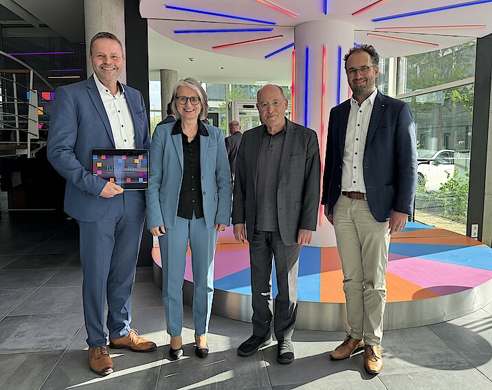 Finanzvorstand Dr. Robert Bachert, Vorstandsvorsitzende Dr. Annette Noller und sozialpolitischer Vorstand Dr. Kornelius Knapp stehen lächelnd neben Gregor Gysi im futurum
